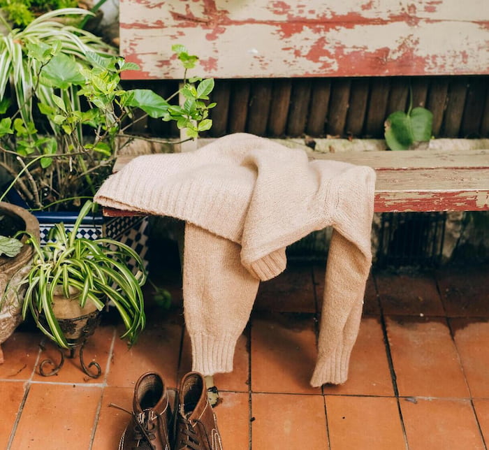 Sweater on a bench and boots on the floor of a greenhouse or mudroom
